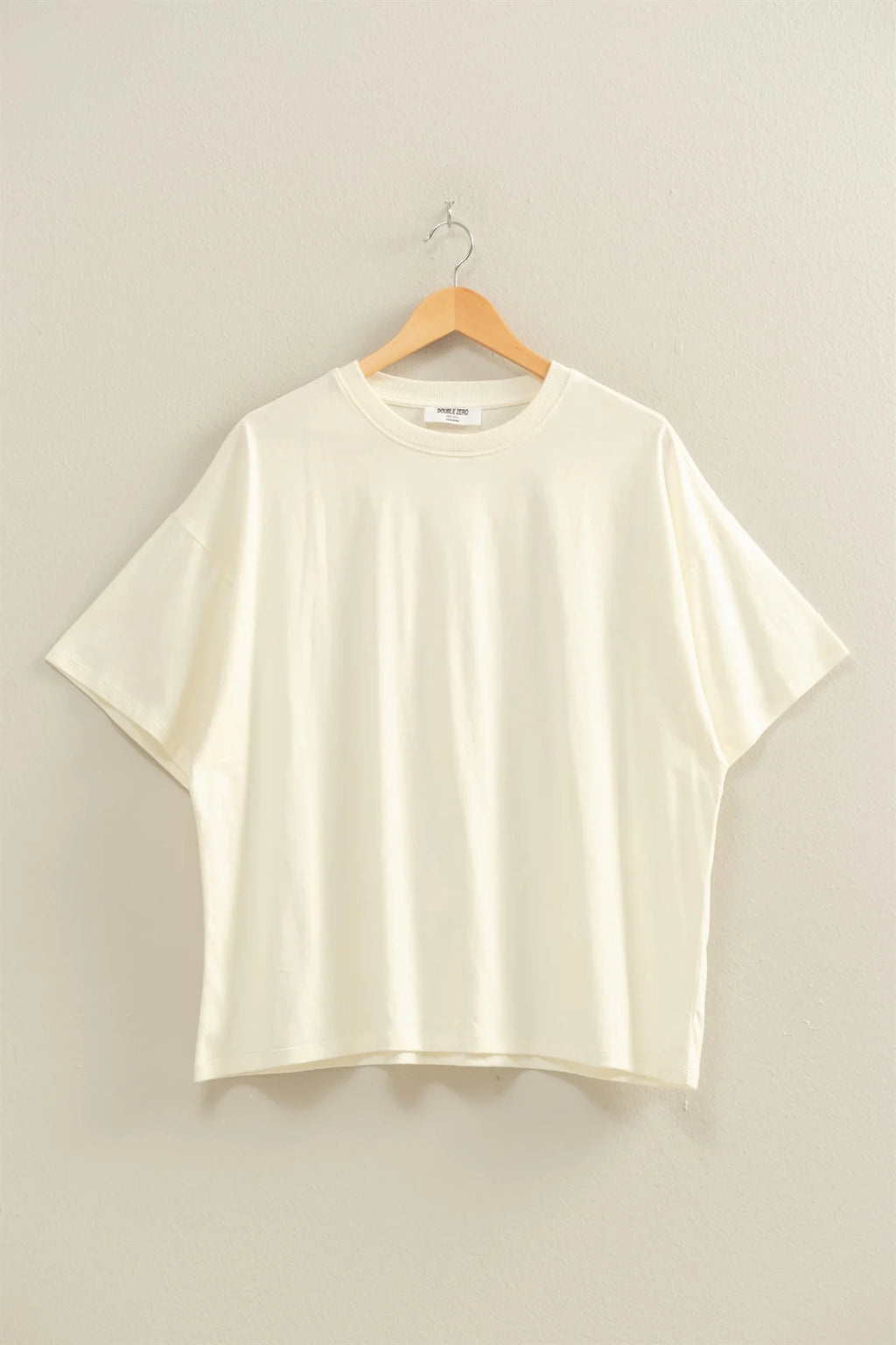 Cream t-shirt on a wooden hanger against a beige background