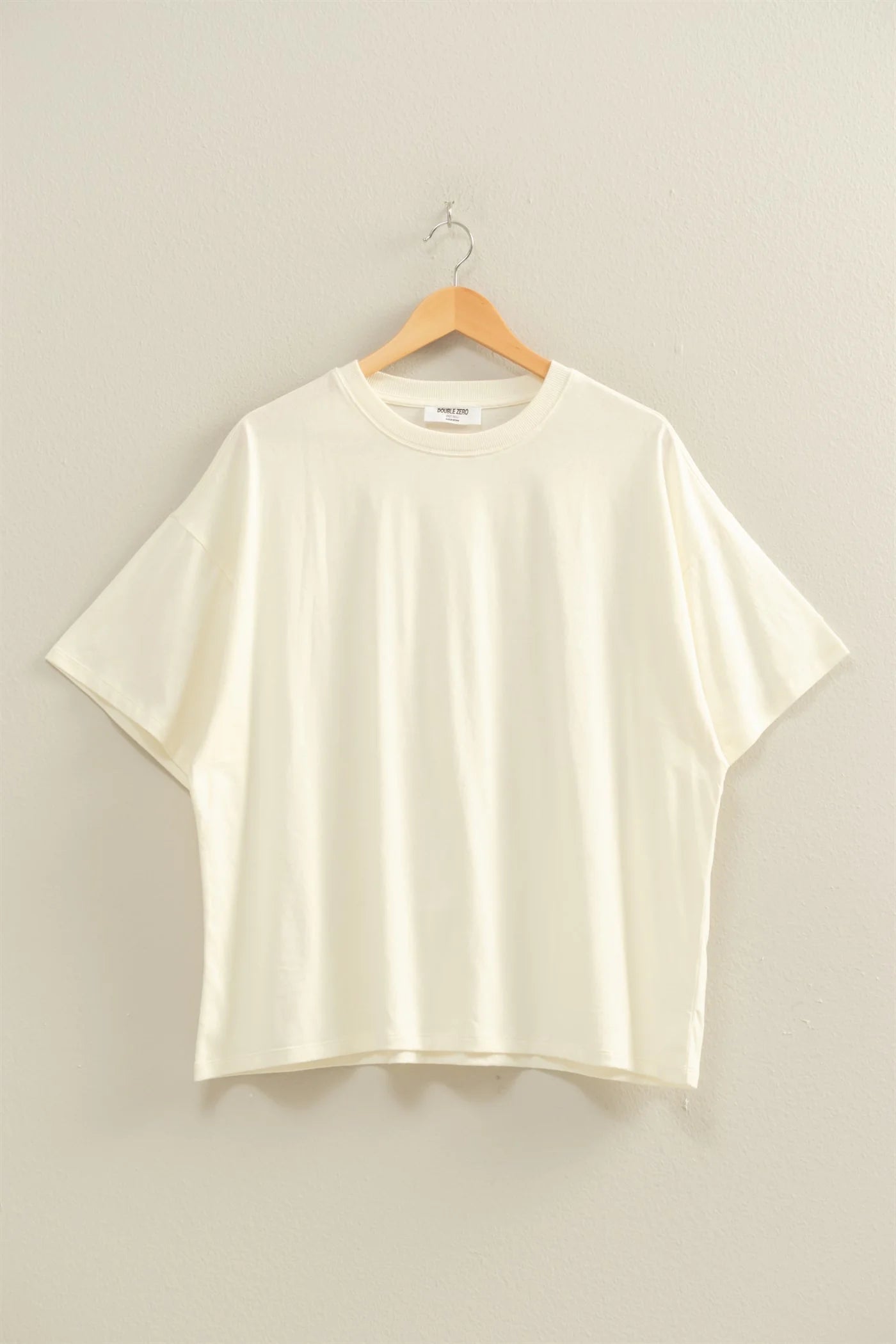 Cream t-shirt on a wooden hanger against a beige background