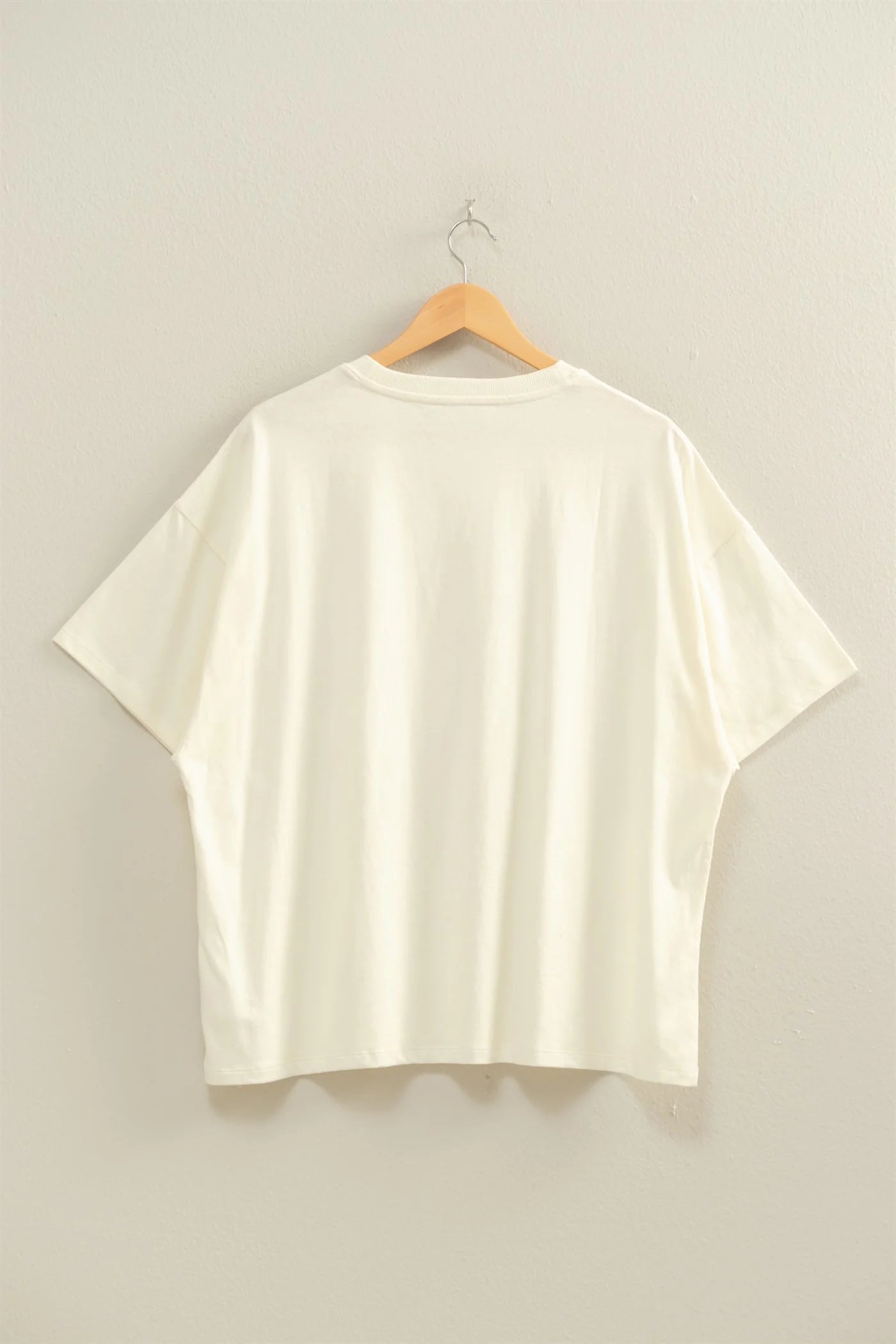 Cream t-shirt on a wooden hanger against a plain background