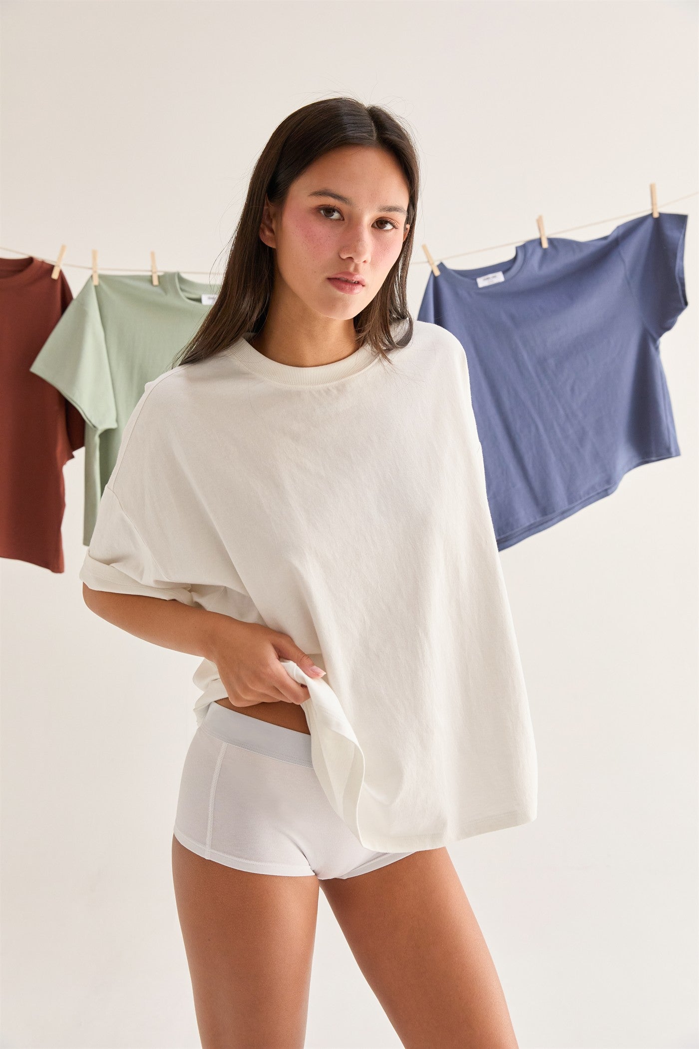 Woman holding a cream t-shirt with clothes hanging in the background