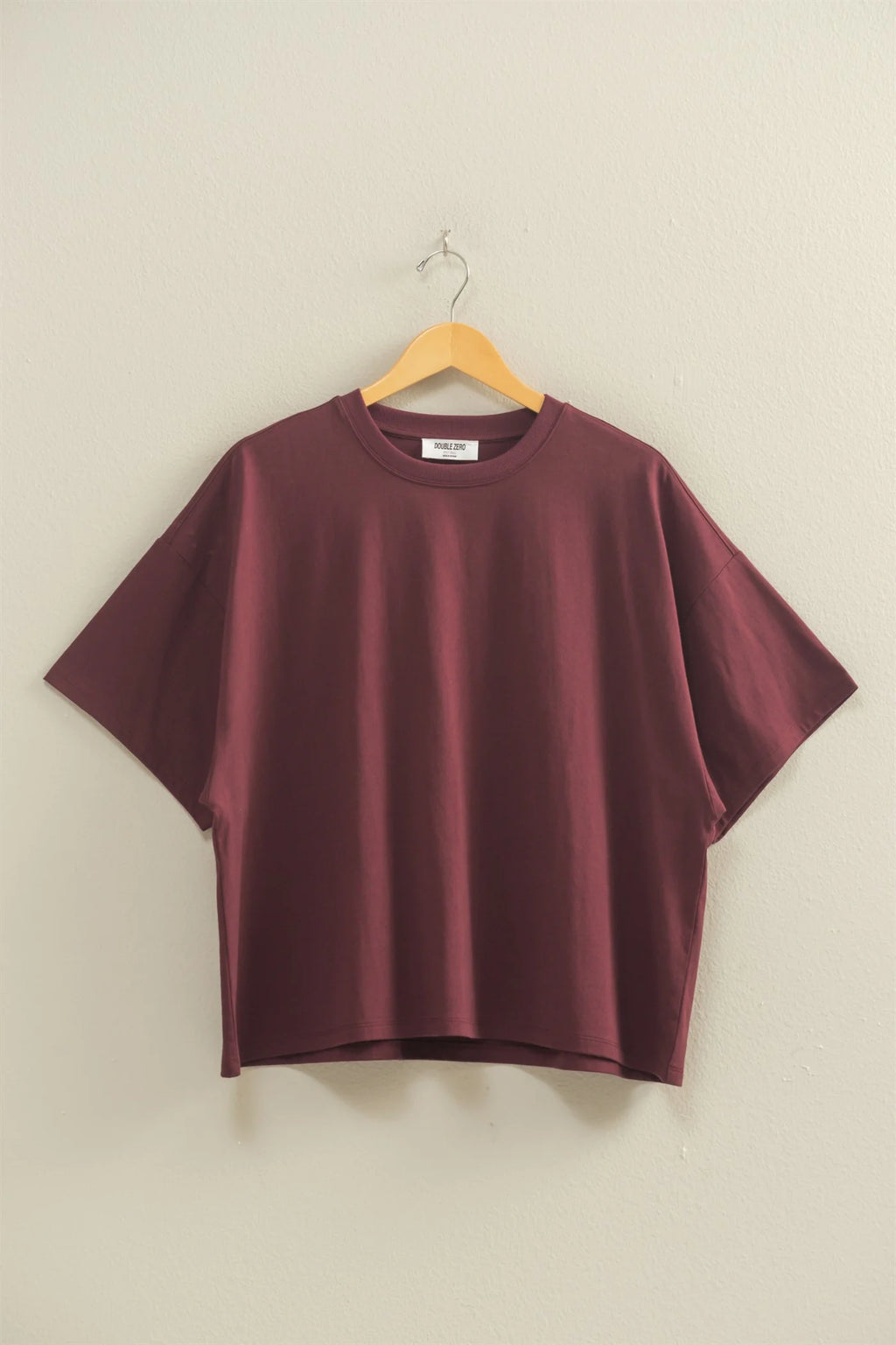 Maroon t-shirt on a wooden hanger against a beige wall