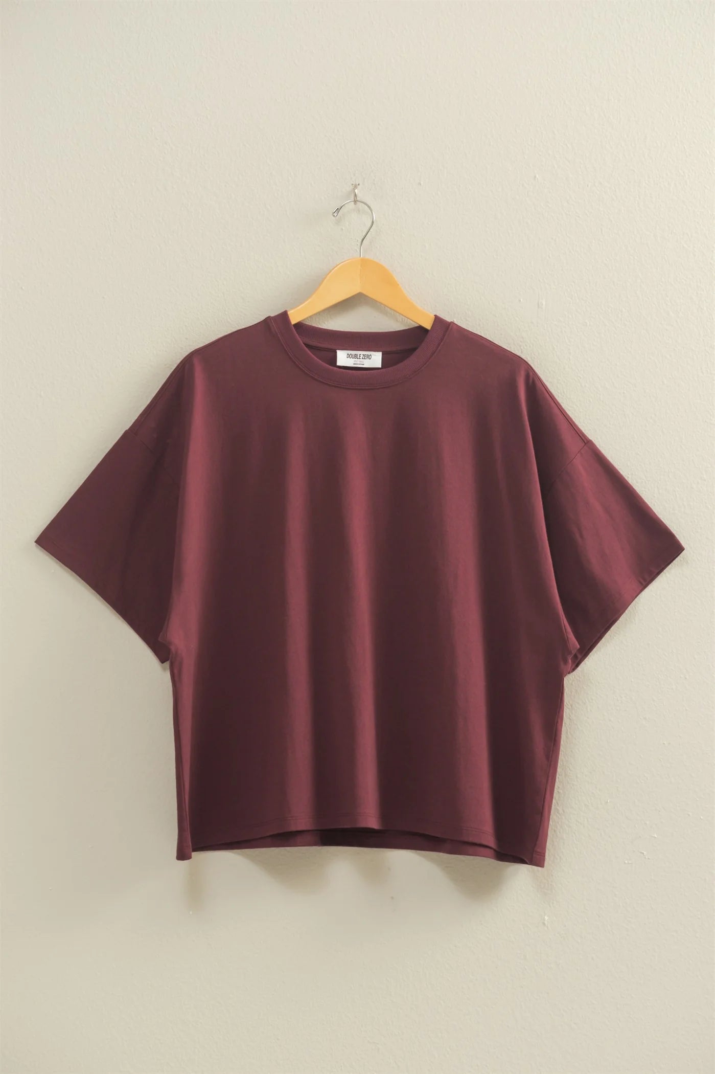 Maroon t-shirt on a wooden hanger against a beige wall