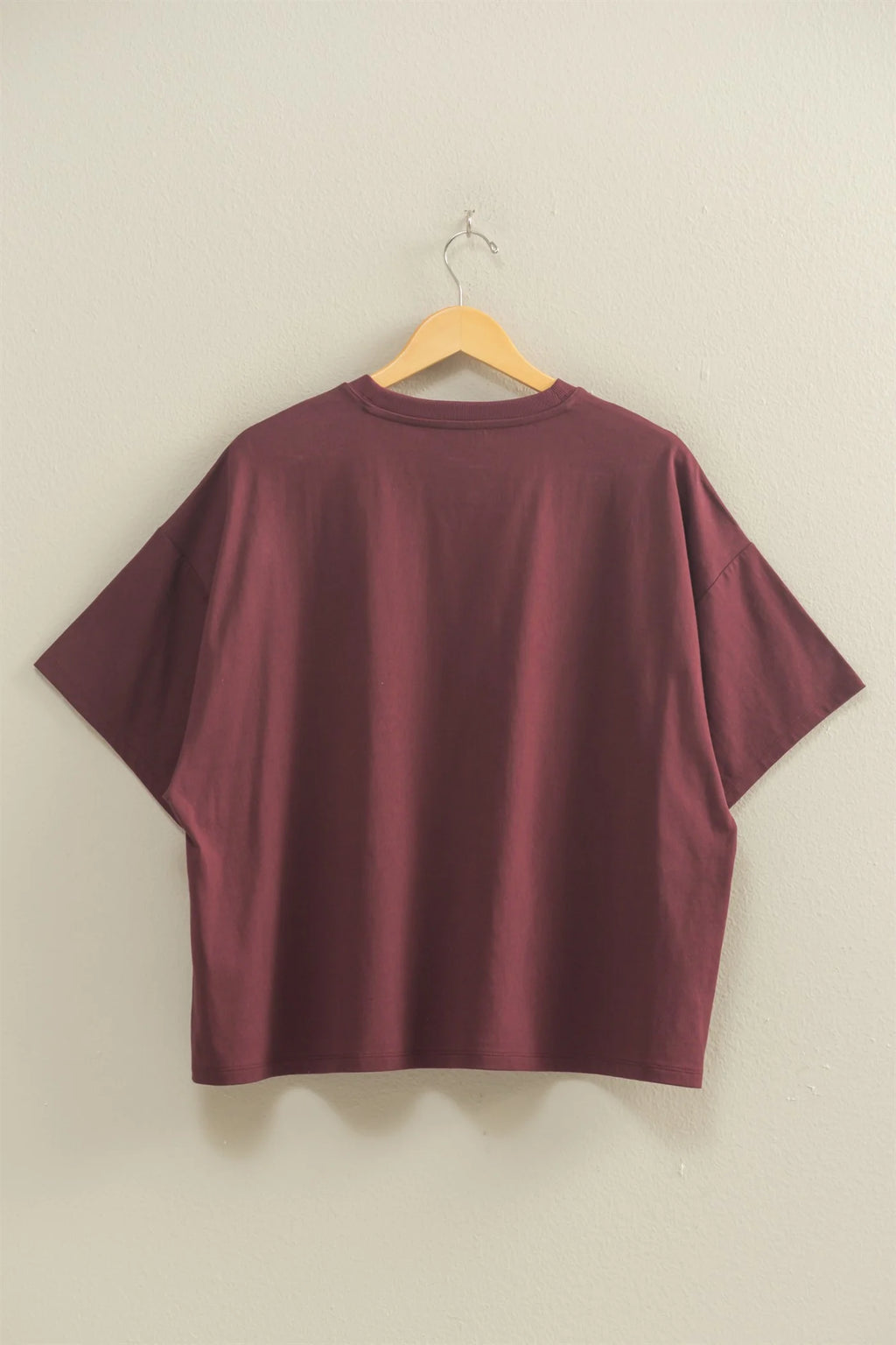 Maroon t-shirt on a wooden hanger against a beige wall