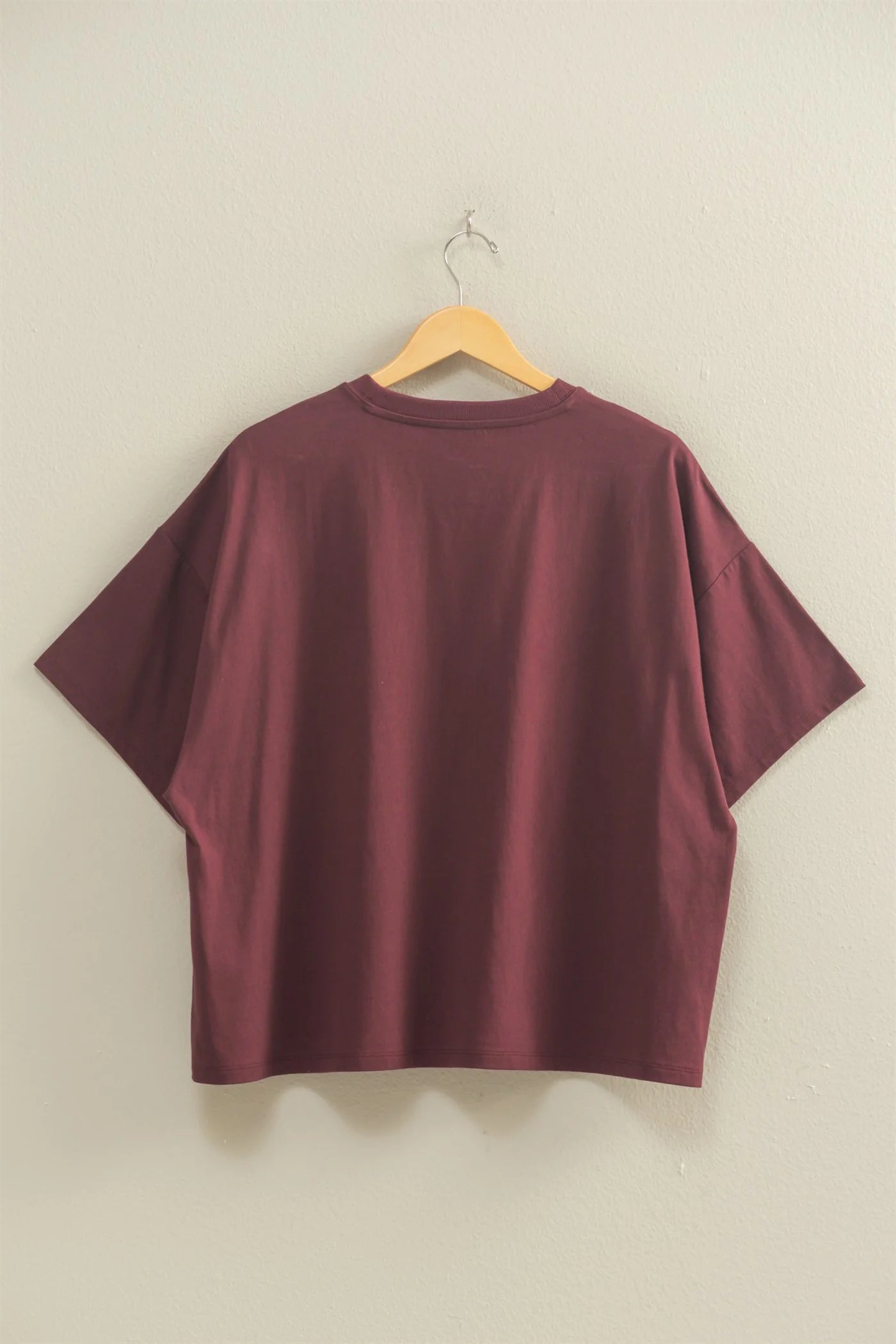 Maroon t-shirt on a wooden hanger against a beige wall