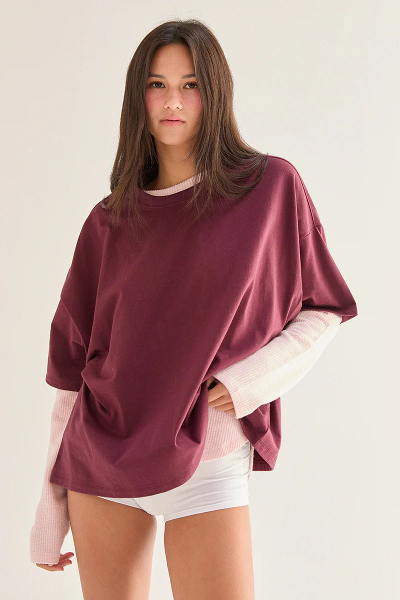 Woman wearing a maroon oversized sweater over a pink shirt on a plain background