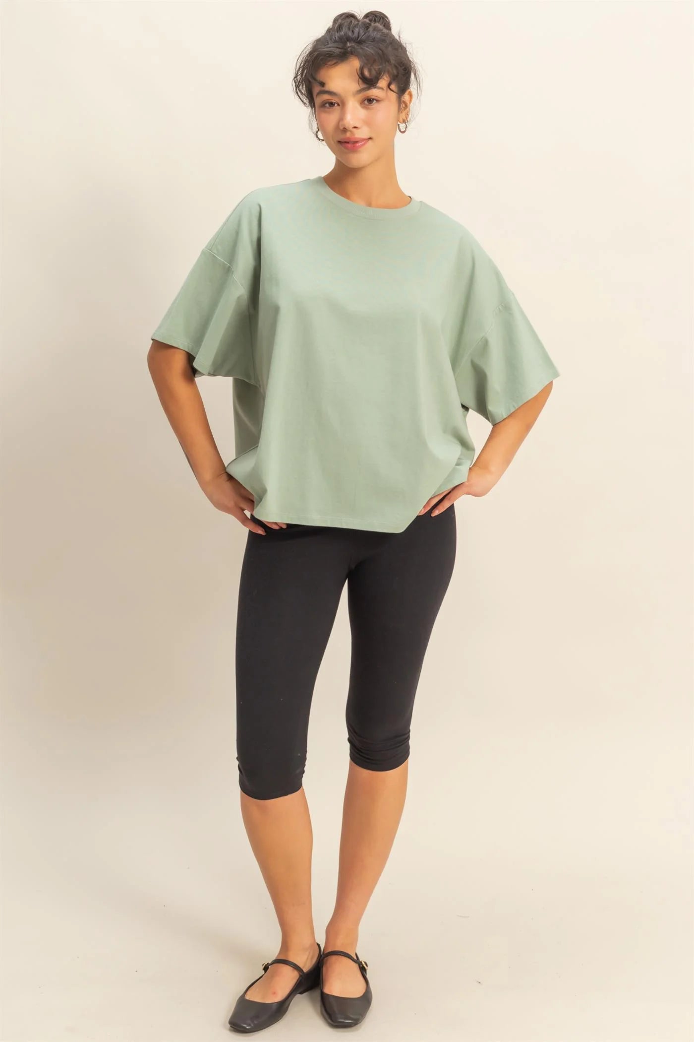 Woman wearing a light green top and black capri pants on a plain background