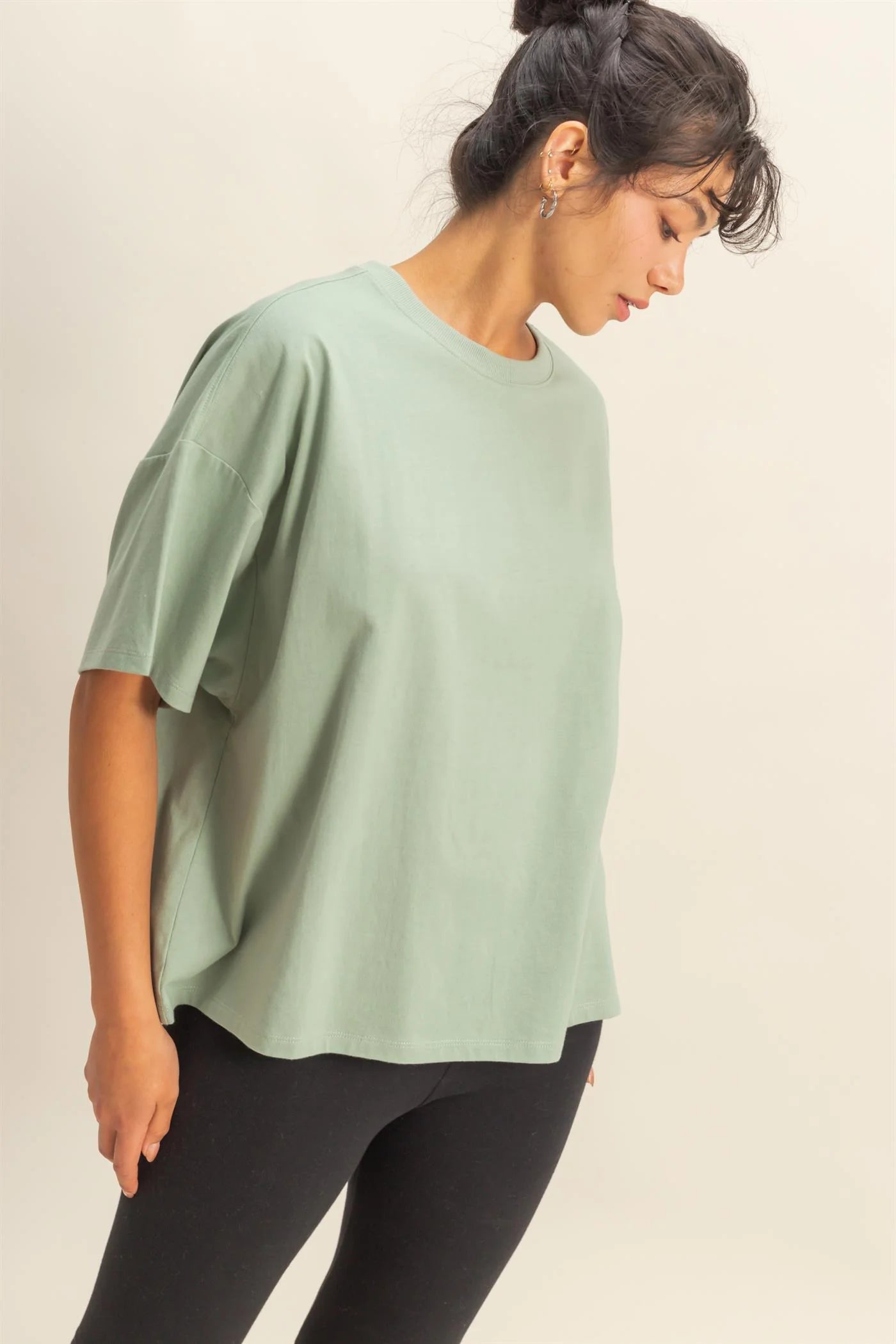 Woman wearing a light green oversized top and black leggings on a plain background